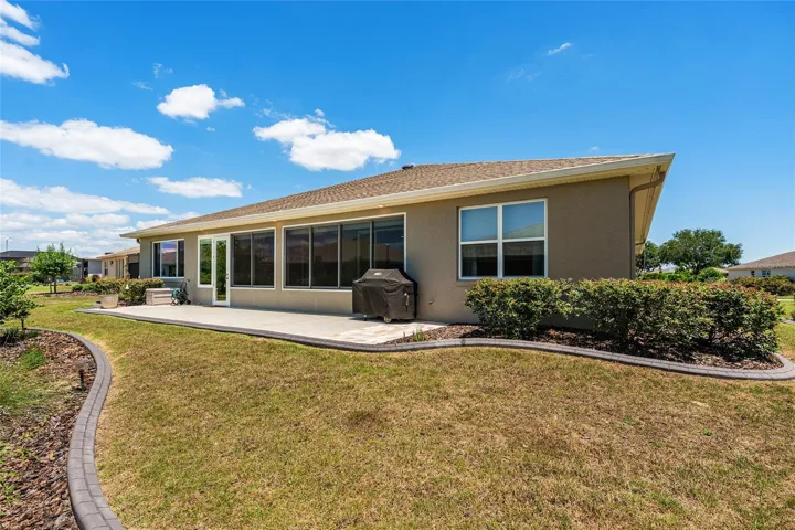 Another view of the spacious rear patio and beautifully landscaped backyard, showcasing concrete curbing, mature plantings, and inviting outdoor space.
