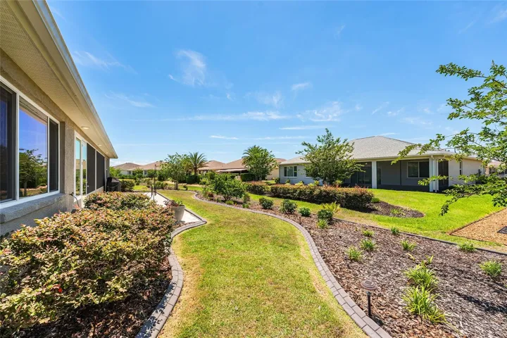Beautiful rear landscaping with concrete curbing, mature plantings, open green space, and a spacious patio area—perfect for enjoying the Florida lifestyle.