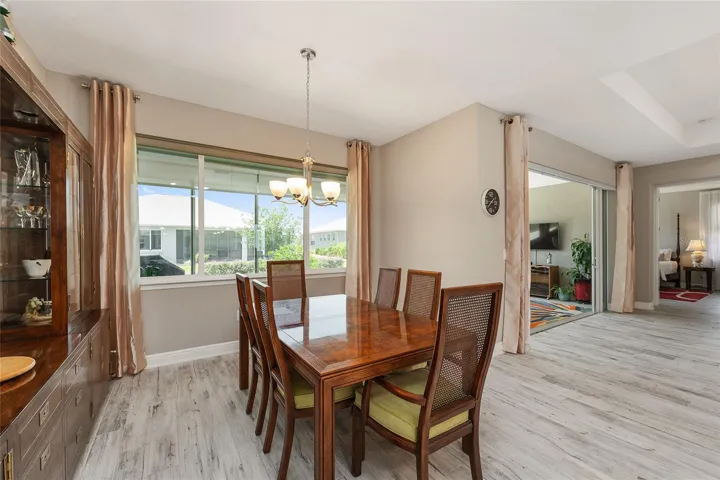 Dining room filled with natural light from large windows, featuring ceramic plank flooring, neutral finishes, and easy flow to the kitchen and great room.