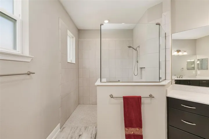 First primary bathroom ensuite with large zero-entry walk-in shower with glass enclosure, tile surround, built-in niche, handheld shower fixture, and spacious design for comfort and convenience.