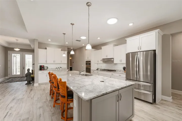 Gorgeous kitchen featuring staggered cabinetry, pull-out drawers, neutral backsplash, two solar tubes, GE gas range, GE dishwasher, LG refrigerator, and an impressive 12’ x 4.5’ Cambria Quartz island with pop-up outlets and extra storage.