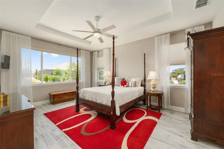 First primary ensuite featuring a tray ceiling, ceiling fan with light, ceramic plank flooring, and multiple windows for beautiful natural light