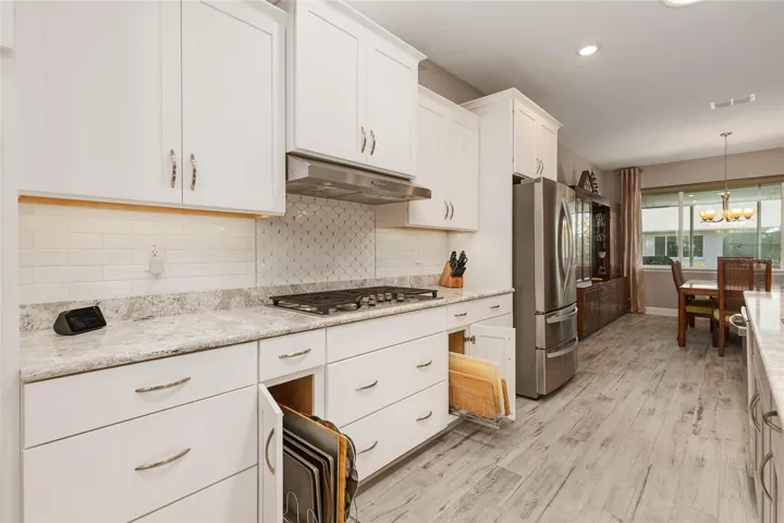 Kitchen view featuring pull-out drawers, neutral backsplash, stainless steel appliances, and open flow to the dining area.