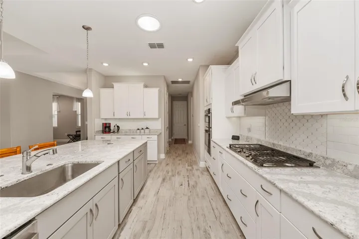 Beautiful kitchen view showcasing staggered cabinetry, neutral backsplash, Cambria Quartz island, ceramic plank flooring, recessed lighting, and a bright open flow to the dining and great room.