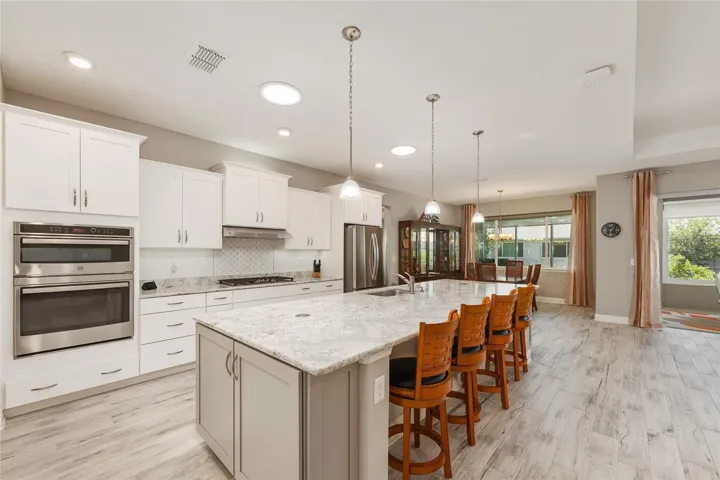 Gorgeous kitchen showcasing a Cambria Quartz island, staggered cabinetry, beautiful wall-mounted microwave and oven, stainless steel appliances, and two solar tubes that brighten the space.