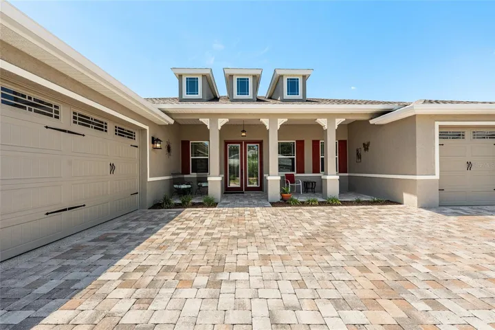 Beautiful 2021 Aberdeen Model showcasing impressive curb appeal with a paver driveway, spacious covered front porch, rich lead glass double-door entry, professional landscaping, and a desirable 3-car garage layout.