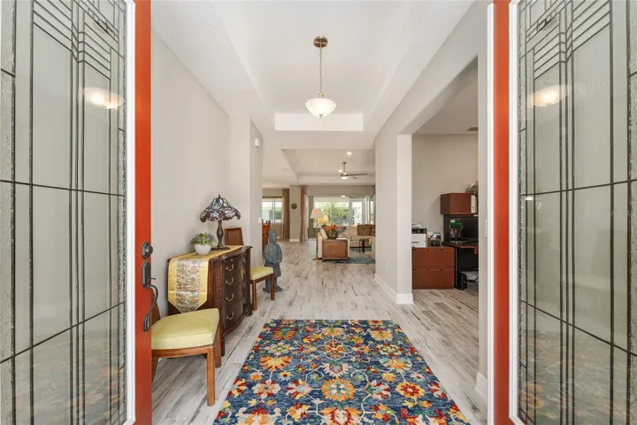 Welcoming foyer featuring lead glass double doors, tray ceiling, ceramic plank flooring, and a bright open feel that sets the tone for this move-in-ready home.