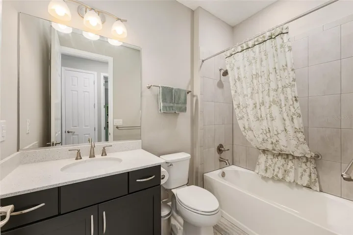 Guest bathroom conveniently located near the third bedroom, featuring a spacious vanity, neutral finishes, bright lighting, and tile tub/shower combination.