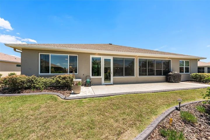 Another rear view highlighting the expansive patio, enclosed lanai, beautiful landscaping, and open green space for outdoor enjoyment.