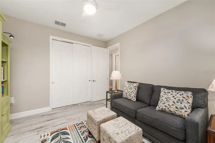 Another view of the third bedroom featuring ceramic plank flooring, ceiling fan with light, neutral finishes, and double sliding closet doors for convenient storage.
