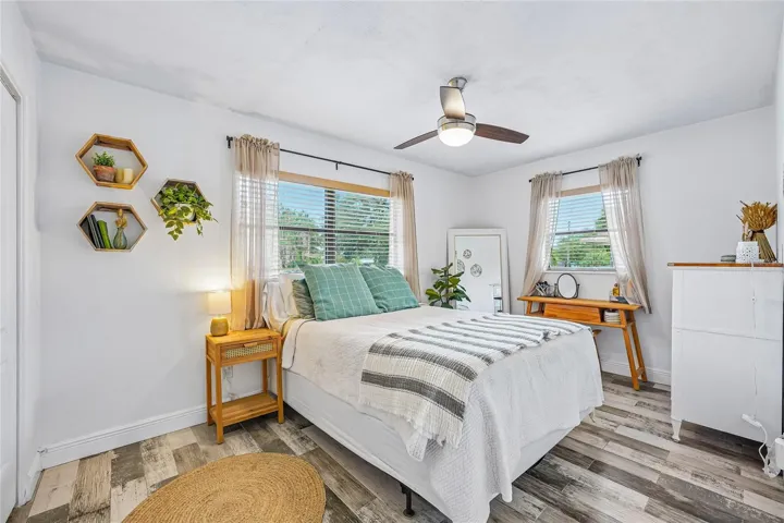 Bedroom 2 — Bedroom with tile flooring, ceiling fan, and two windows with blinds and sheer curtains. Hexagonal wall shelves and natural light throughout.
