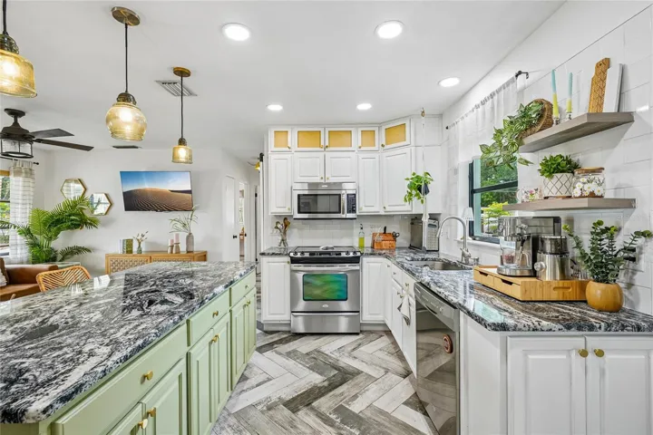 Kitchen — Kitchen with white cabinetry, dark granite countertops, subway tile backsplash, stainless steel range, built-in microwave, and open floating shelves. Green beadboard island with matching granite countertop and amber glass pendant lights above.