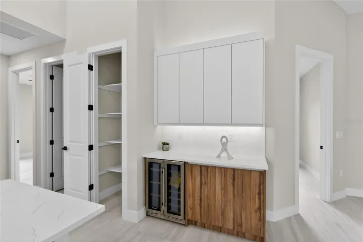 Built-in BUTLER’S PANTRY w/ warm WOOD-GRAIN cabinetry, sleek WHITE upper cabinets, QUARTZ countertops, under-cabinet lighting & built-in WINE REFRIGERATOR, ideal for BEVERAGE STATION, COFFEE BAR, or EXTRA STORAGE & PREP SPACE.