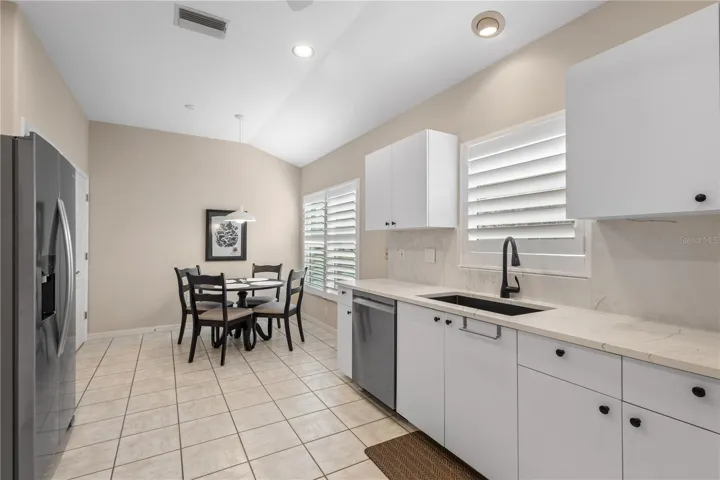 Bright and open kitchen featuring upgraded quartz countertops, plantation shutters, vaulted ceilings, and a cheerful breakfast nook