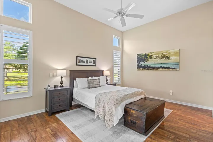 Spacious primary suite with soaring ceilings, rich flooring, plantation shutters, and peaceful lake views that create a bright and relaxing retreat