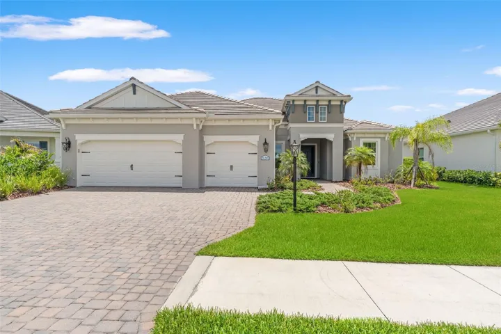 Beautiful British West Indies-inspired elevation with manicured landscaping, paver driveway, and spacious three-car garage.