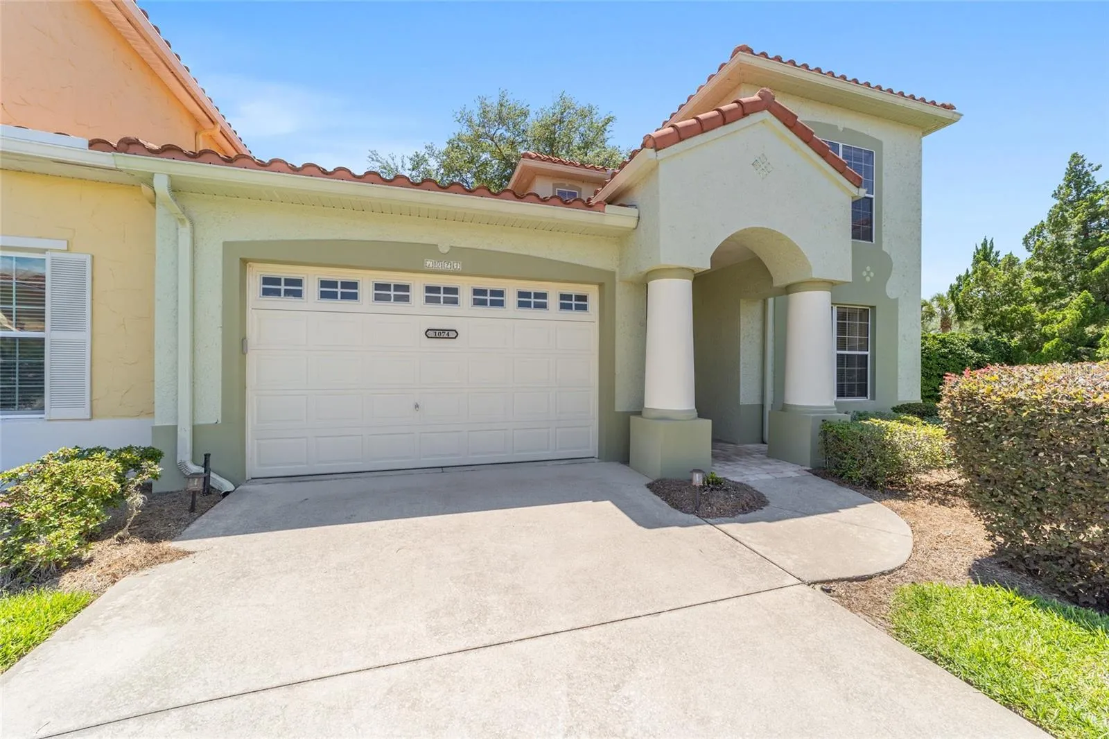 Garage & Entry Exterior – Covered front entry and attached garage are framed by decorative columns and tile roofing, offering both style and functionality. The paved walkway and landscaped surroundings enhance the home’s exterior presentation.