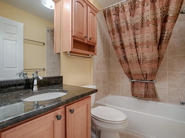 GUEST BATHROOM WITH TILE SURROUND TUB/SHOWER, GRANITE COUNTER, AND TILE FLOORING. THE LINEN CLOSET IS IN THE HALLWAY.