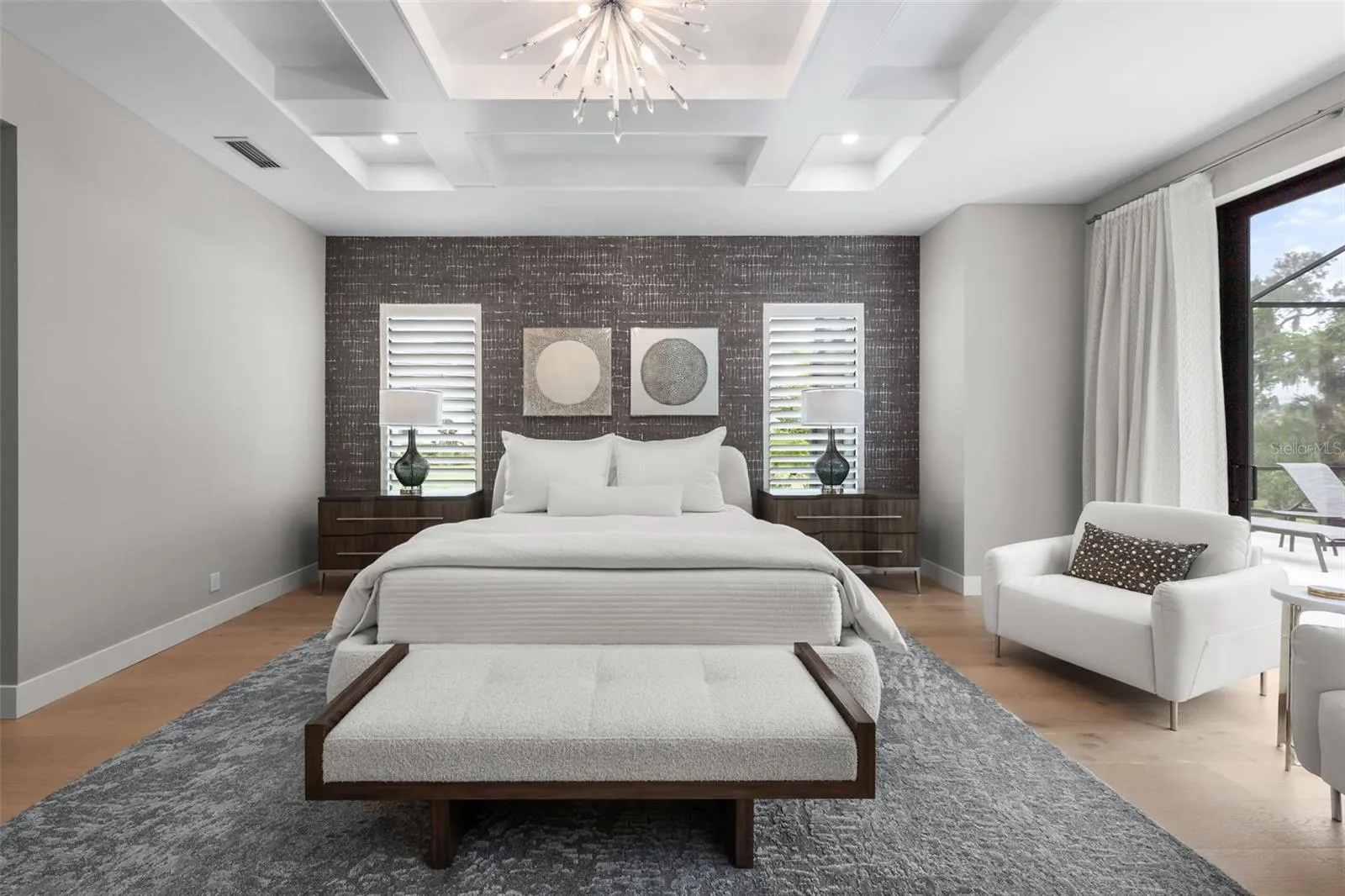 Coffered ceilings with recessed lighting, designer wallpaper accents, and an elegant chandelier create a calming yet sophisticated atmosphere.