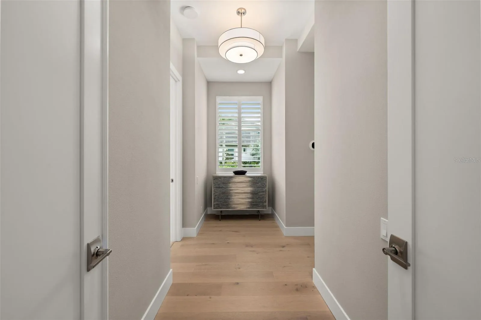 The entry way to the primary suite has double doors, beautiful lighting and a window overlooking the beautifully landscaped yard.
