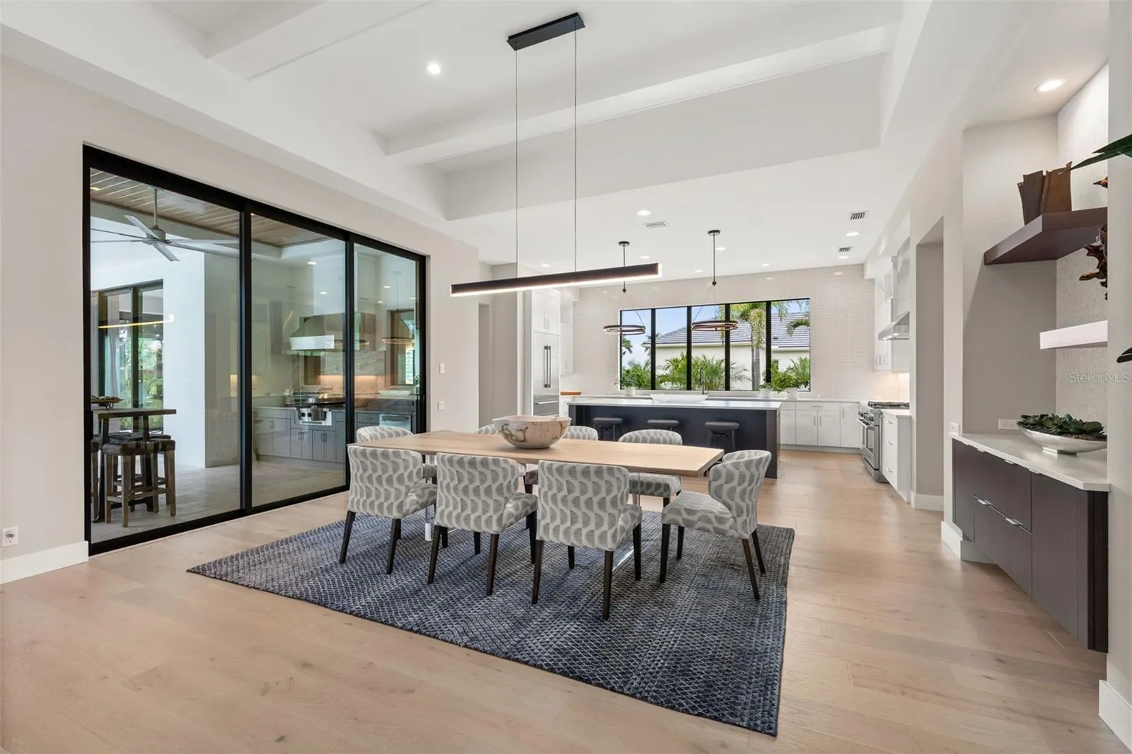 The adjacent dining room is refined, featuring a Schonbek Beyond Mystique LED linear pendant and glass sliding doors with access to the outdoor kitchen and covered lanai.