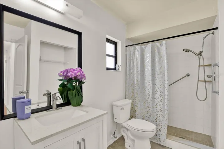 Tastefully updated guest bathroom featuring a crisp white vanity and a spacious, walk in shower.