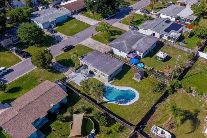 High-angle backyard aerial view capturing the home’s gated patio area, detached storage shed, privacy fencing, and refreshing pool.