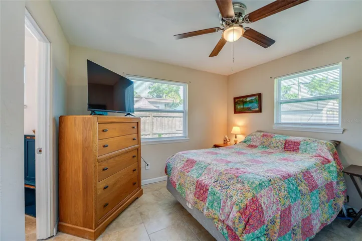 Cozy bedroom featuring warm tan walls, tile flooring, and ample natural light from two windows.