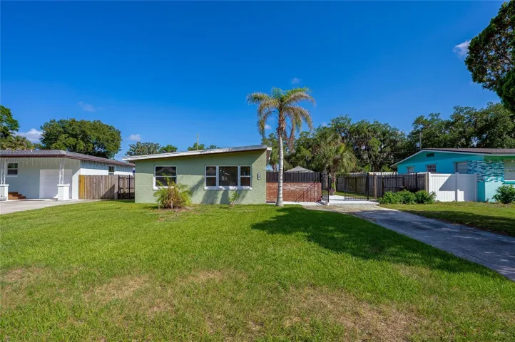 Front exterior of a charming, light green mid-century modern home showcasing a distinctive sloped roofline, a manicured lawn, and a palm tree.
