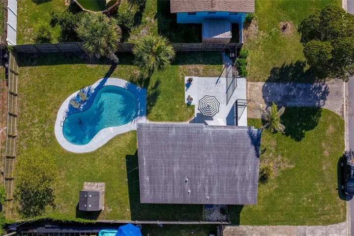 Direct top-down aerial view detailing the property's layout, including the home’s roof, a paved patio with a seating area, an immaculate lawn, and a swimming pool.