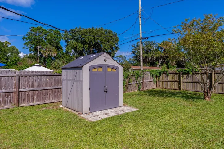Fully fenced backyard featuring a spacious, modern storage shed set on a paved foundation.