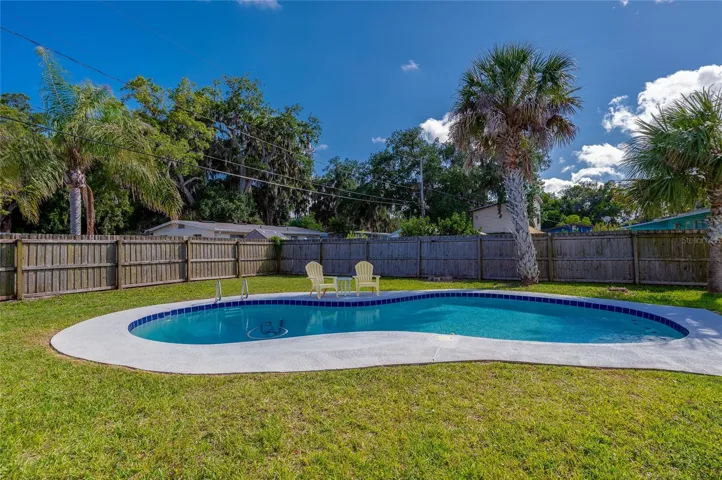 Serene poolside setting framed by a tall wooden privacy fence and a backdrop of lush, tropical foliage.