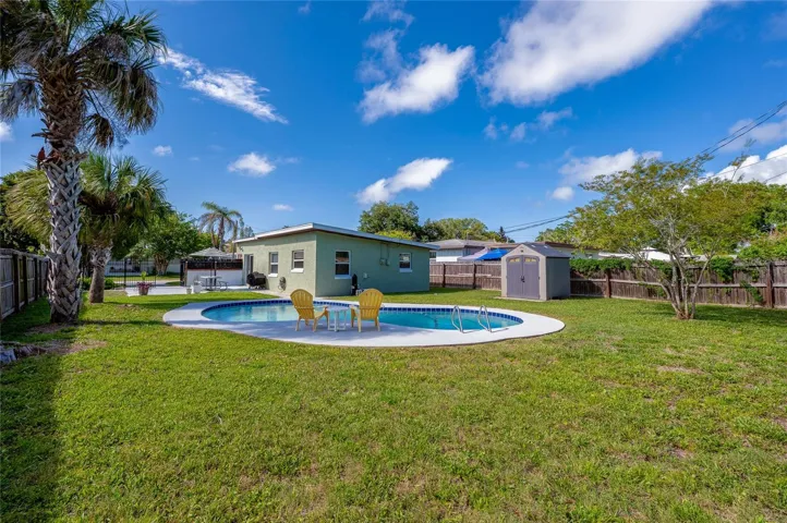Generous backyard view showcasing the home's green exterior, a detached storage shed, and a poolside seating area.