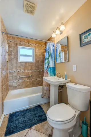Full bathroom accented by floor-to-ceiling  wall tiles, a classic pedestal sink, and a combination bathtub and shower.
