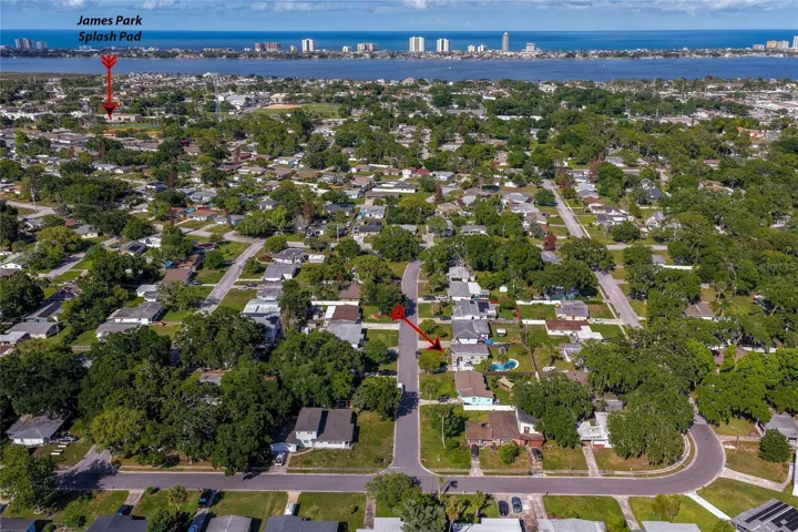 Wide aerial perspective highlighting the property’s location within the neighborhood, with a red arrow pointing toward the home and another local attractions and nearby coastal waters.