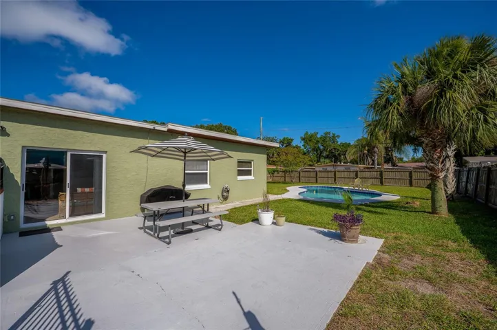 Inviting concrete patio area perfect for outdoor dining, overlooking a spacious green lawn and a private, sparkling in-ground pool.
