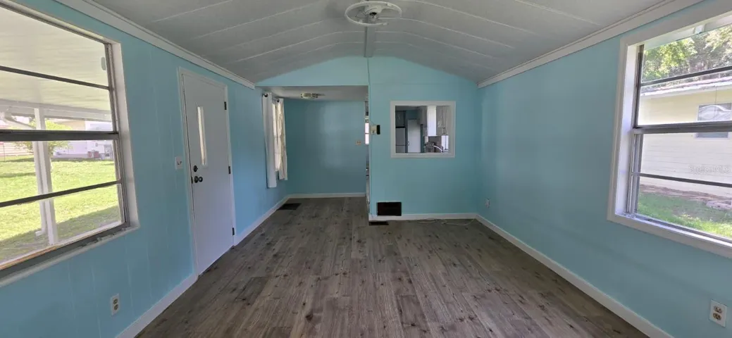 Living Room — Front Door Looking In"Step inside and the vaulted ceiling opens everything up. New LVP flooring, soft coastal walls, and natural light flooding in from both sides — it feels bigger than the square footage suggests.