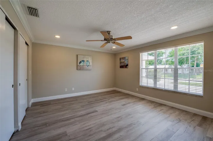 Generously sized primary bedroom complete with crown molding, double closets, an updated ceiling fan, and a wide window looking out to the yard.