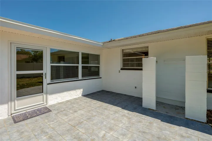 A charming tiled patio space offers the perfect spot for outdoor seating and relaxation just outside the back door. The area features clean stucco walls and large windows.