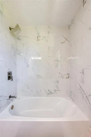 Updated shower and tub combination featuring sleek, modern hardware and elegant marble-style tile surround.
