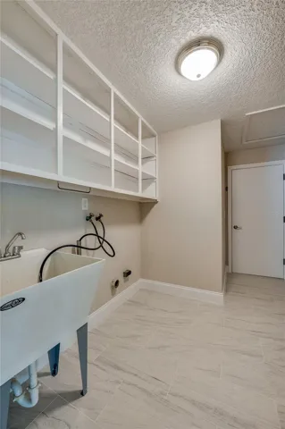 Practical laundry room equipped with built-in overhead storage shelves and a deep utility sink. The space is neatly designed making it an ideal setup for laundry.