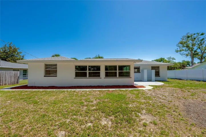 The rear exterior of the home showcases fresh white paint, large glass windows that invite natural light inside, and a neat border of red landscaping mulch. The spacious backyard offers plenty of room for future outdoor additions or recreation.