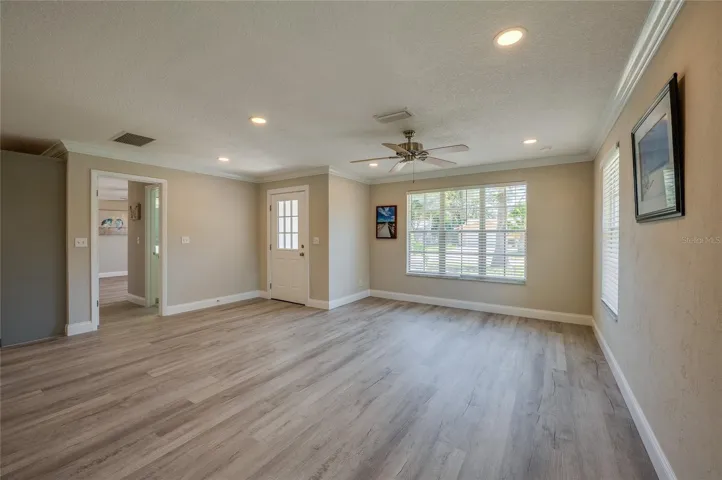 Welcoming entryway and living area boasting neutral walls, vinyl flooring, and large windows that invite plenty of natural light. A classic ceiling fan helps keep the open space cool and comfortable.