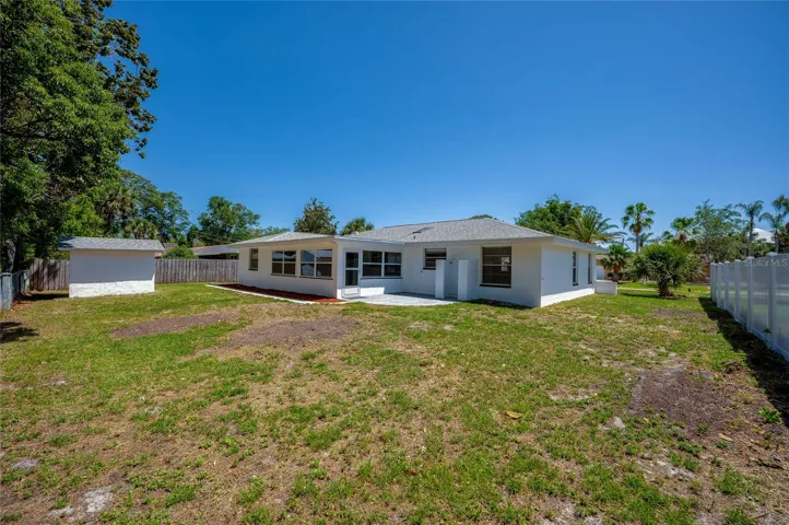 The expansive backyard provides a wide stretch of green lawn, fully enclosed by combination wood and chain link privacy fencing. A detached storage shed stands ready to house lawn equipment or tools.