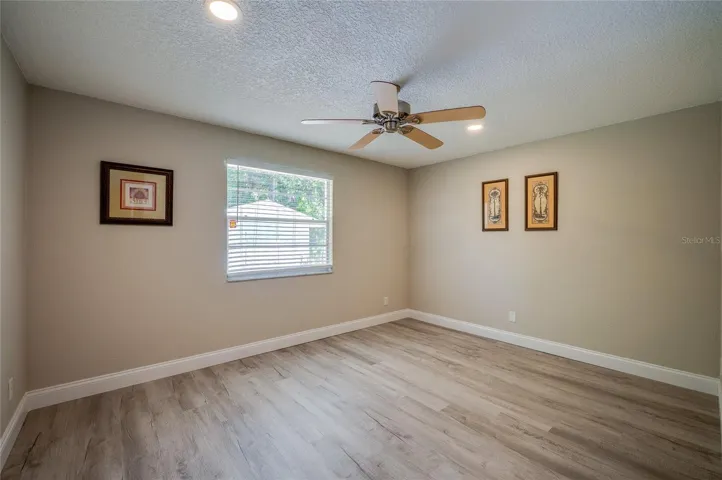 Spacious bedroom highlighted by clean lines, a large window letting in natural light, a ceiling fan, and durable vinyl flooring.