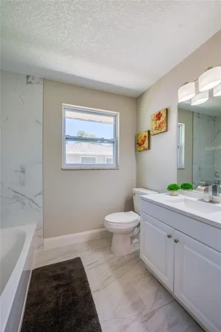 Modern bathroom equipped with a white vanity, floor-to-ceiling marble- tiled shower/tub, and a bright window that fills the space with natural light.