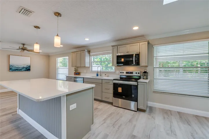Stylish kitchen prep area highlighted by crisp countertops, a modern tile backsplash, and sleek stainless steel cooking appliances. Multiple windows provide a pleasant view of the outdoors while flooding the workspace with natural light.