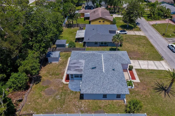 An elevated aerial view highlighting the property's architectural rooflines and its connection to the deep backyard space. The shot captures the home's patio layout, dedicated storage shed, and the dense tree line providing an excellent natural privacy buffer along the property border.