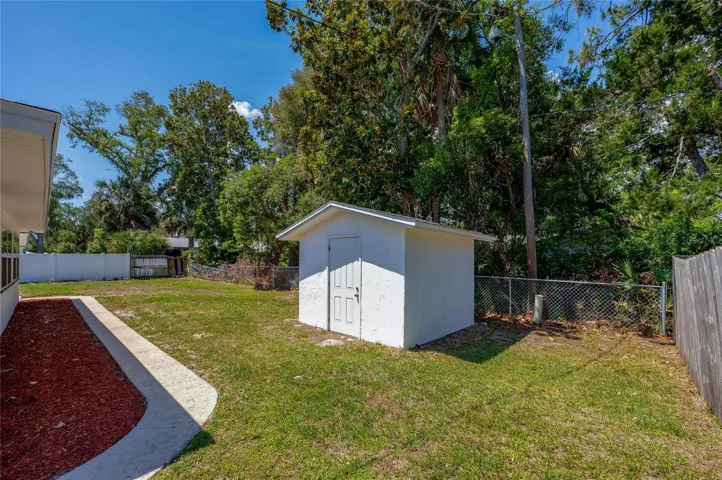 This side perspective highlights the generous length of the backyard, accented by a concrete walkway and a fresh mulch border along the home. The secure fencing and towering trees ensure plenty of privacy from neighbors.
