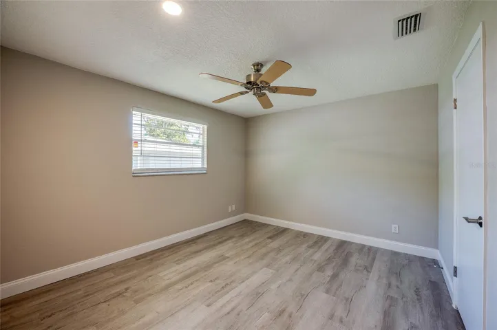 Comfortable bedroom featuring matching vinyl flooring, neutral wall tones, and an integrated ceiling fan. A bright window and clean baseboards complete this cozy, private retreat.